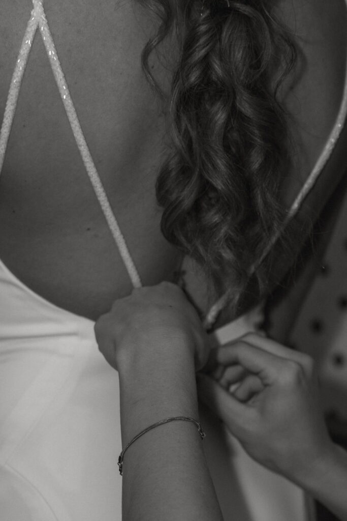 black and white photo closeup of bridesmaid zipping up morgans wedding dress