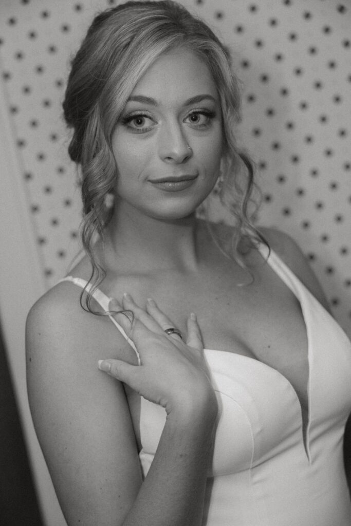 black and white serious close up of bride looking at camera in her wedding dress at getting ready location, right hand on her right shoulder wedding dress strap.