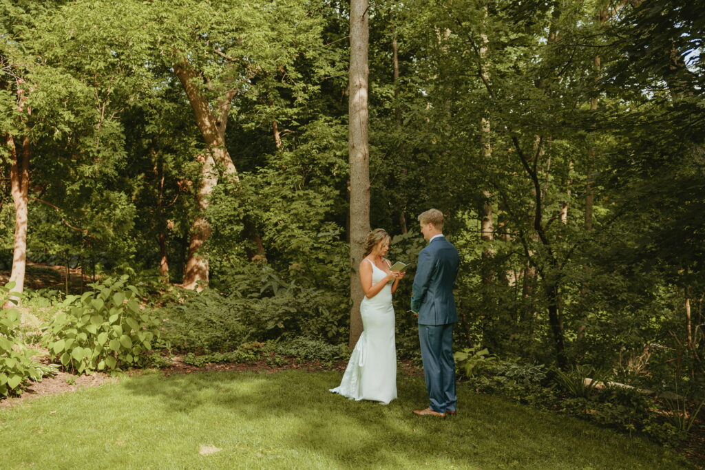 morgan and grant during their first look surrounded by nature in grooms parents backyard reading their vows