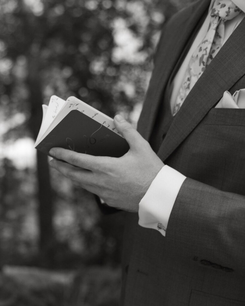 groom flipping page during vows at wedding in black and white side view