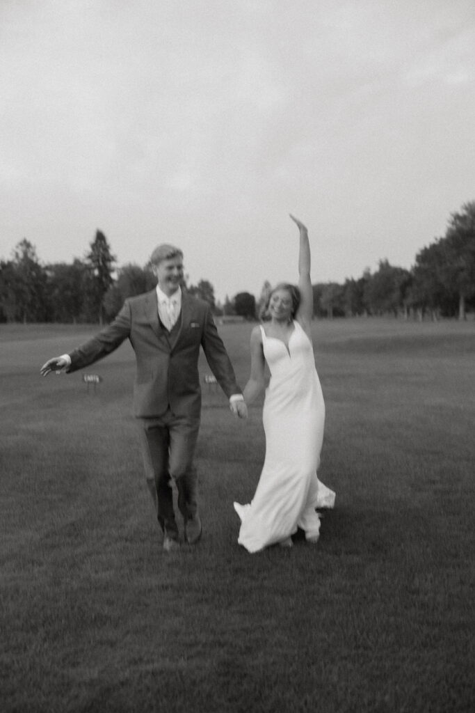 black and white photo of couple cheerfully running toward camera at Butte des morts on golf course