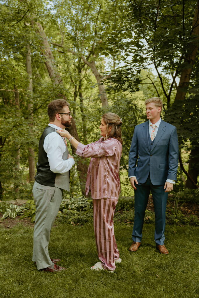grooms mom helping his brother fix tie and groom looking over from the side of them all ready for wedding