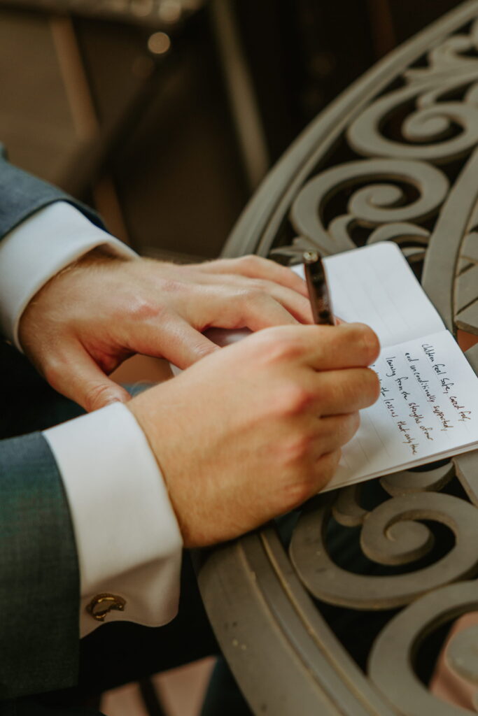 close up of groom writing his vows morning of wedding outside on patio furniture