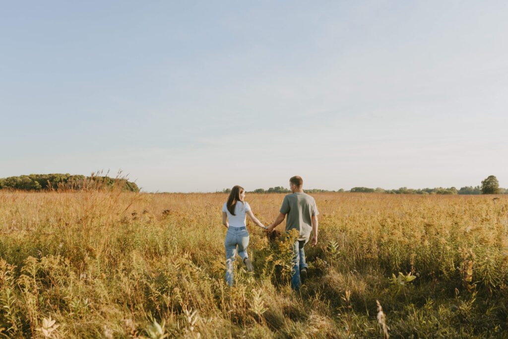 couple walking away from camera for engagement pictures in a field in luxemburg wisconsin
