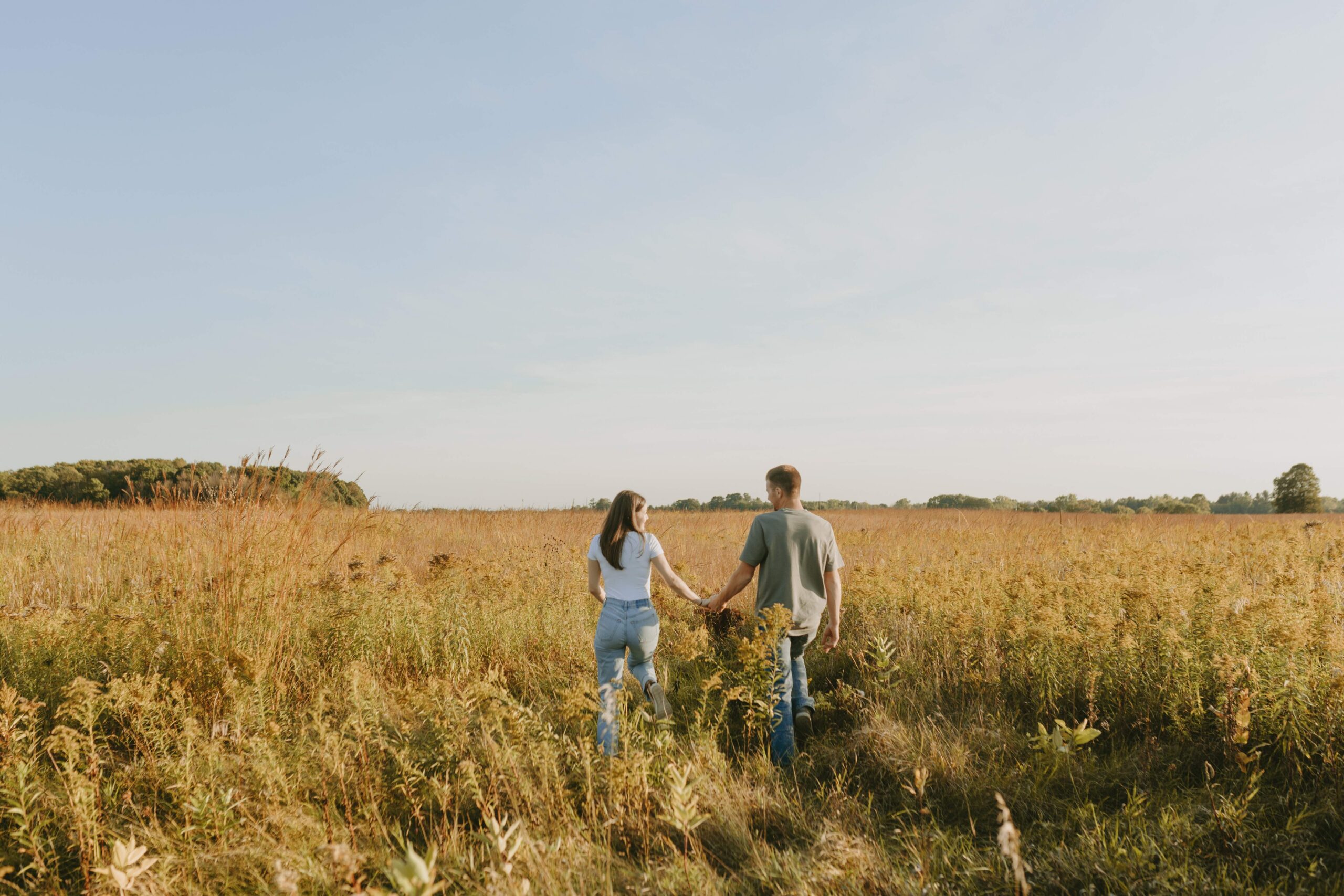 couple walking away from camera for engagement pictures in a field in luxemburg wisconsin