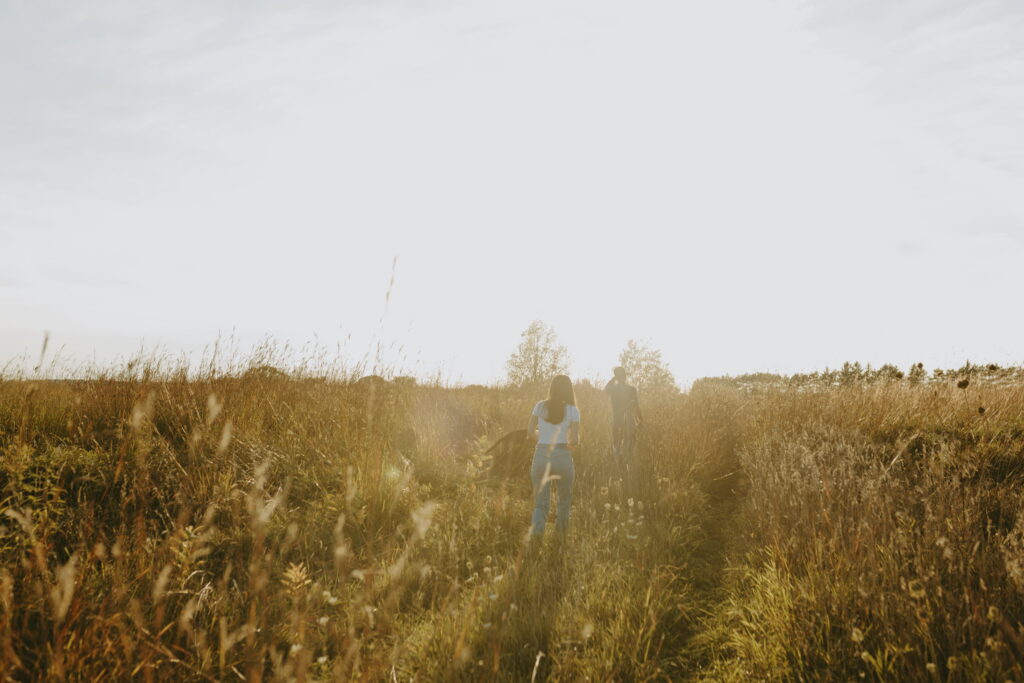 couple walking away with dog with golden hour shining so you can barely see them. artsy engagement shoot type of vibe!