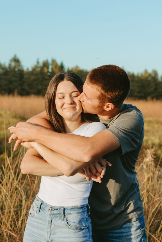 couple engagement pics with arms around eachother kissing her cheek