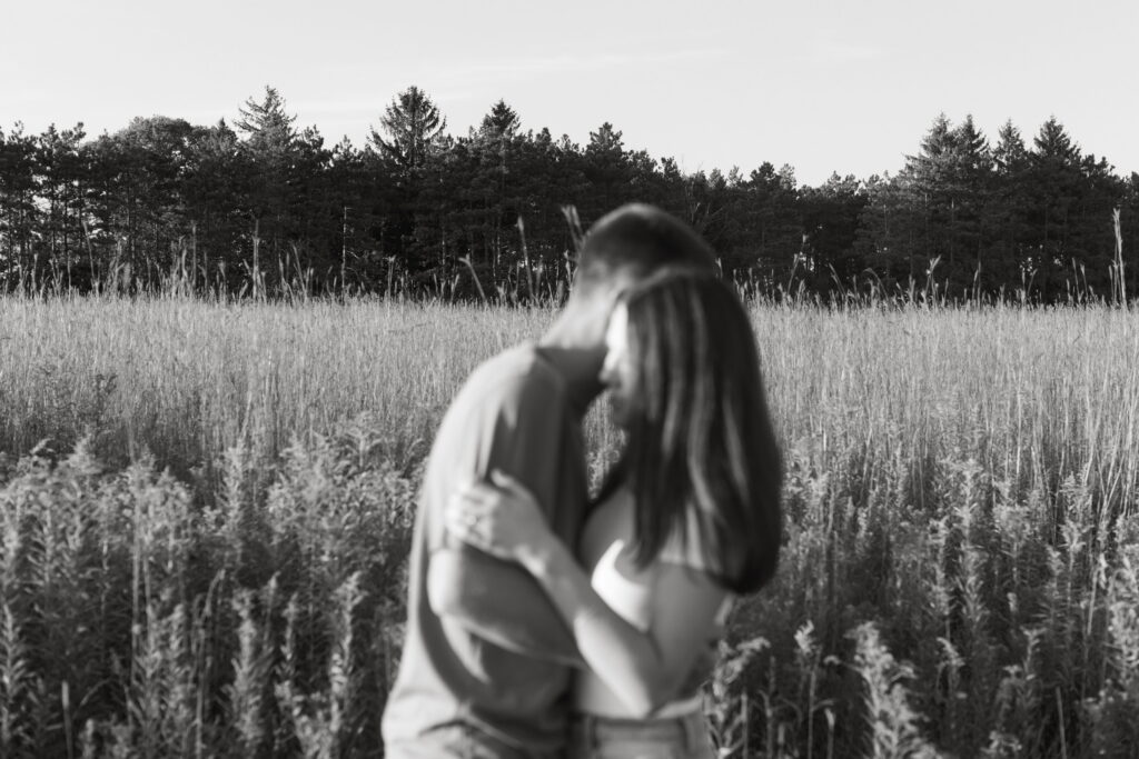 black and white photo of couple during engagement shoot. couple is blurry and background is in focus in a random Wisconsin field
