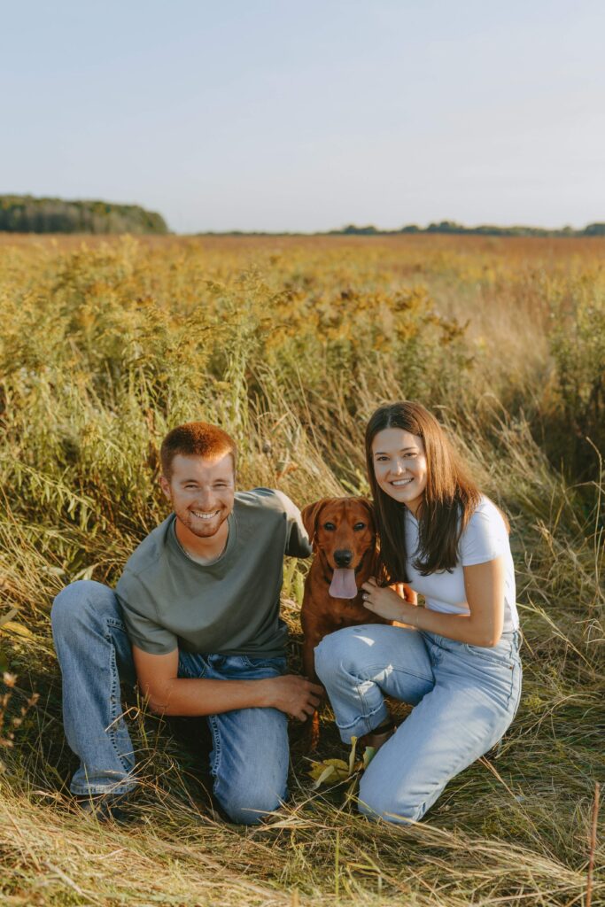 couple hanging out in a wisconsin field for engagement photos with their dog