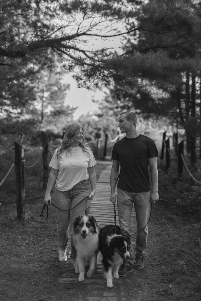 black and white photo of couple with their dogs at kohler andrae on trail
